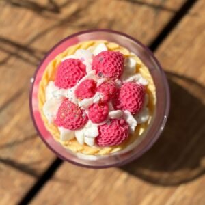 Vue du dessus de la bougie artisanale Fruits Rouges MURI, décorée de framboises roses en cire et de crème fouettée brillante