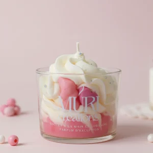 Bougie gourmande artisanale Muri Créations parfum Amour de bébé, présentée avec une cire fouettée façon chantilly blanche et des cœurs roses, coulée à la main en Lorraine aux notes douces et poudrées.