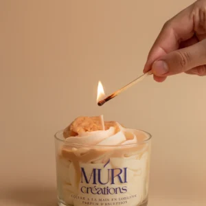 Main craquant une allumette pour allumer la mèche d'une bougie gourmande éclats de cookie de la marque artisanale Muri Créations, caractérisée par sa cire fouettée et son topping biscuit réaliste.