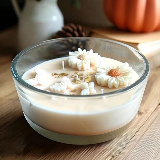 Bougie artisanale XXL 800ml avec fleurs blanches, papillons en cire et feuilles d’or, dans un verre rond sur une table en bois