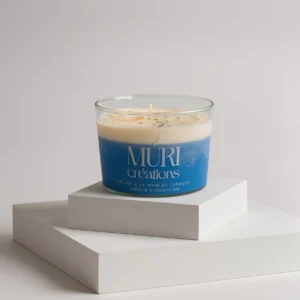 Bougie parfumée artisanale Muri Créations à la senteur fleur de coton, avec une cire bicolore bleue et crème dans un verre, posée sur des socles blancs minimalistes.