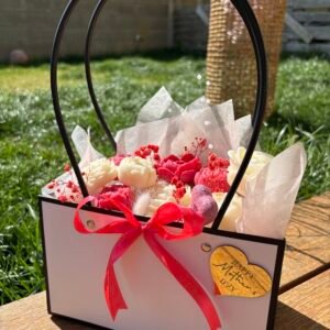 Bouquet de fondants parfumés artisanaux présenté dans un sac rigide blanc avec ruban rouge, photographie en extérieur sur table en bois – Muri Créations
