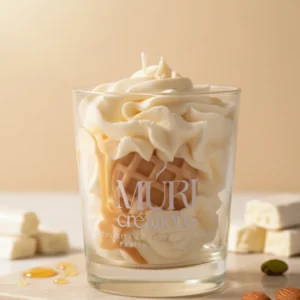 Bougie parfumée au nougat de la marque artisanale Muri Créations, présentée dans un verre avec une cire effet chantilly, un insert gaufrette et un coulis caramel, entourée de morceaux de nougat blanc, d'amandes et de pistaches.