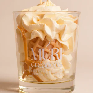 Bougie parfumée au nougat de la marque artisanale Muri Créations, présentée dans un verre transparent avec une cire gourmande fouettée façon chantilly, agrémentée d'une gaufrette et d'un coulis caramel.
