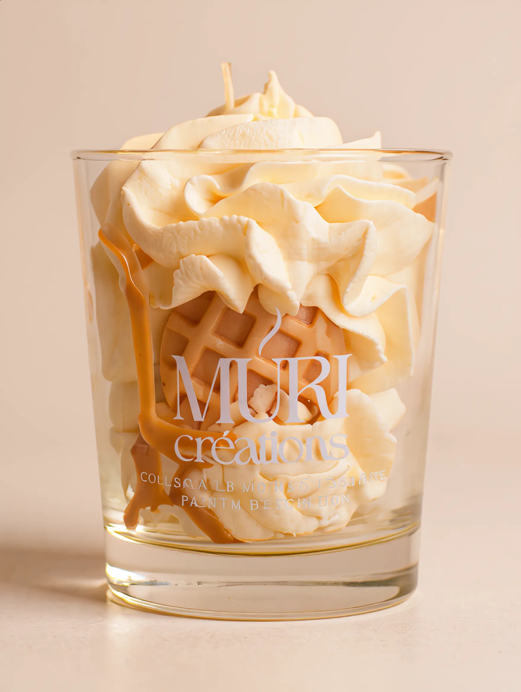 Bougie parfumée Nougat Blanc 2 Bougie parfumée au nougat de la marque artisanale Muri Créations, présentée dans un verre transparent avec une cire gourmande fouettée façon chantilly, agrémentée d'une gaufrette et d'un coulis caramel.